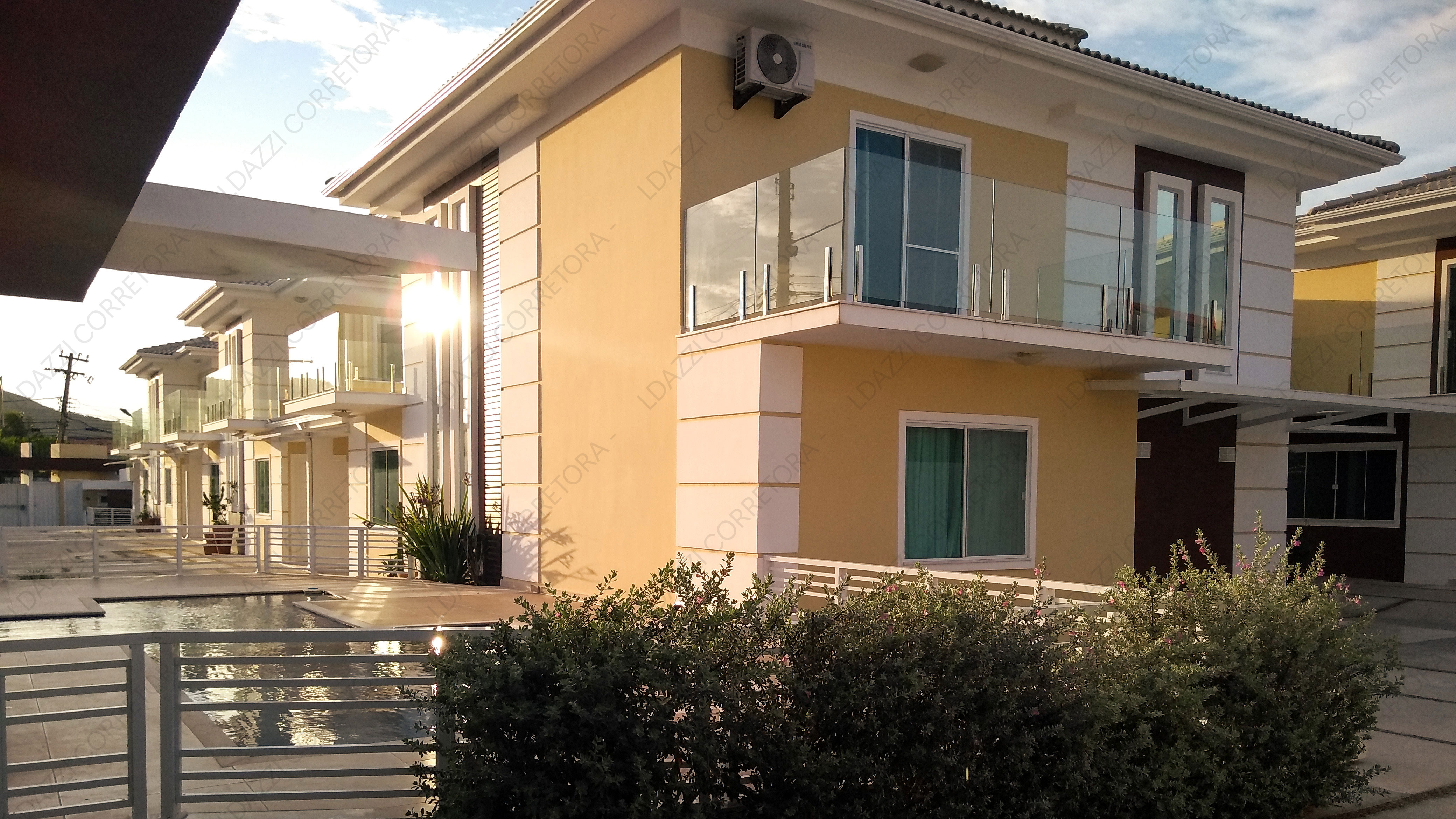 Fachada da casa vista lateralmente e piscina do condominio no por do sol.